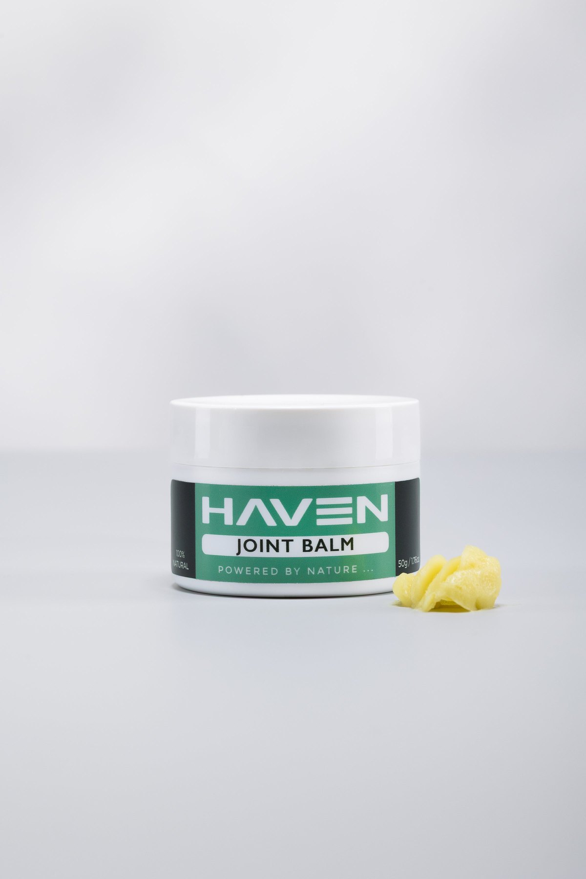 A closed jar of Haven Joint Balm with a portion of the yellow balm beside it, on a pale studio background